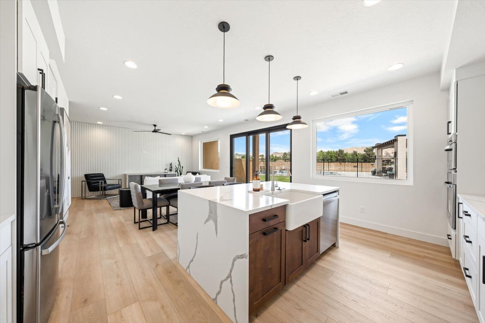Modern kitchen featuring a waterfall island with a farmhouse sink, stainless steel appliances, and wood-finish flooring