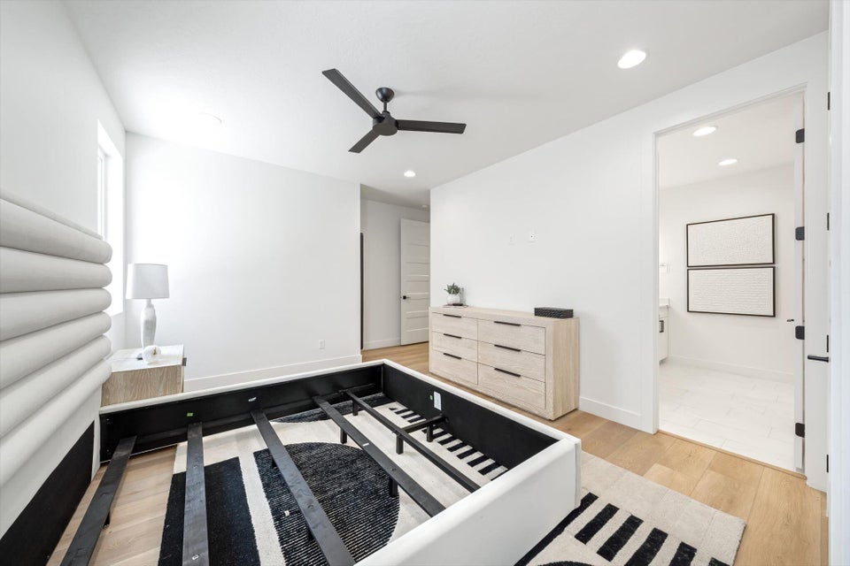 Bright room featuring light wood-finish flooring, white walls, and a black ceiling fan