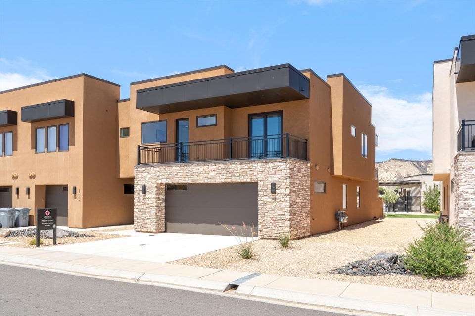 Modern exterior featuring a stacked stone facade, integrated garage, upper-level balcony with black railing, and contemporary windows