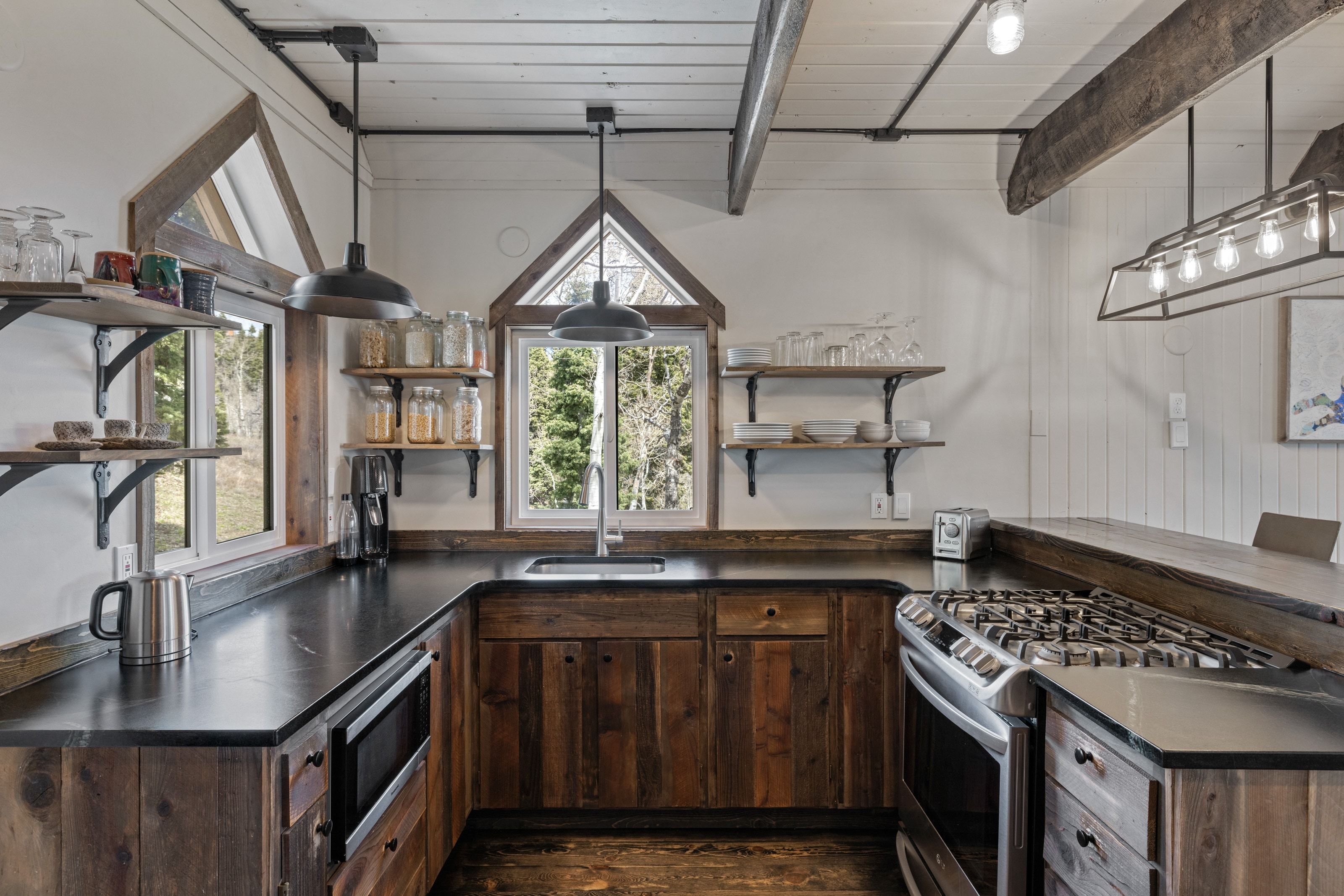 Kitchen featuring dark countertops, open shelves, dark wood finish cabinets, stainless steel appliances, and a wood ceiling with exposed beams