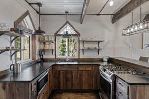 Kitchen featuring dark countertops, open shelves, dark wood finish cabinets, stainless steel appliances, and a wood ceiling with exposed beams