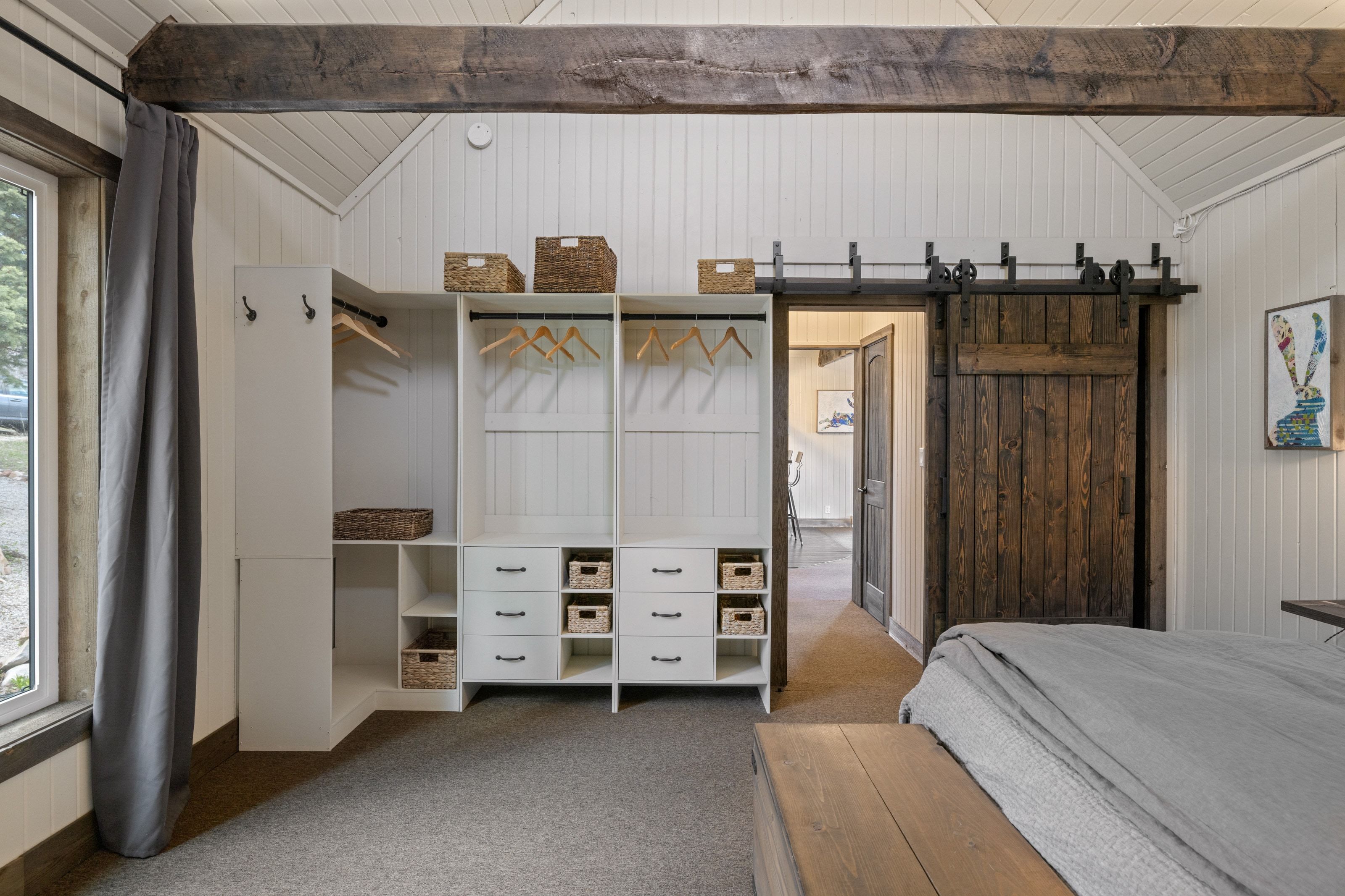 Bedroom with a barn door, light colored carpet, vaulted ceiling, and wooden walls