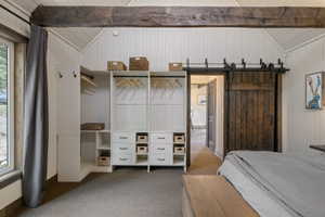 Bedroom with a barn door, light colored carpet, vaulted ceiling, and wooden walls