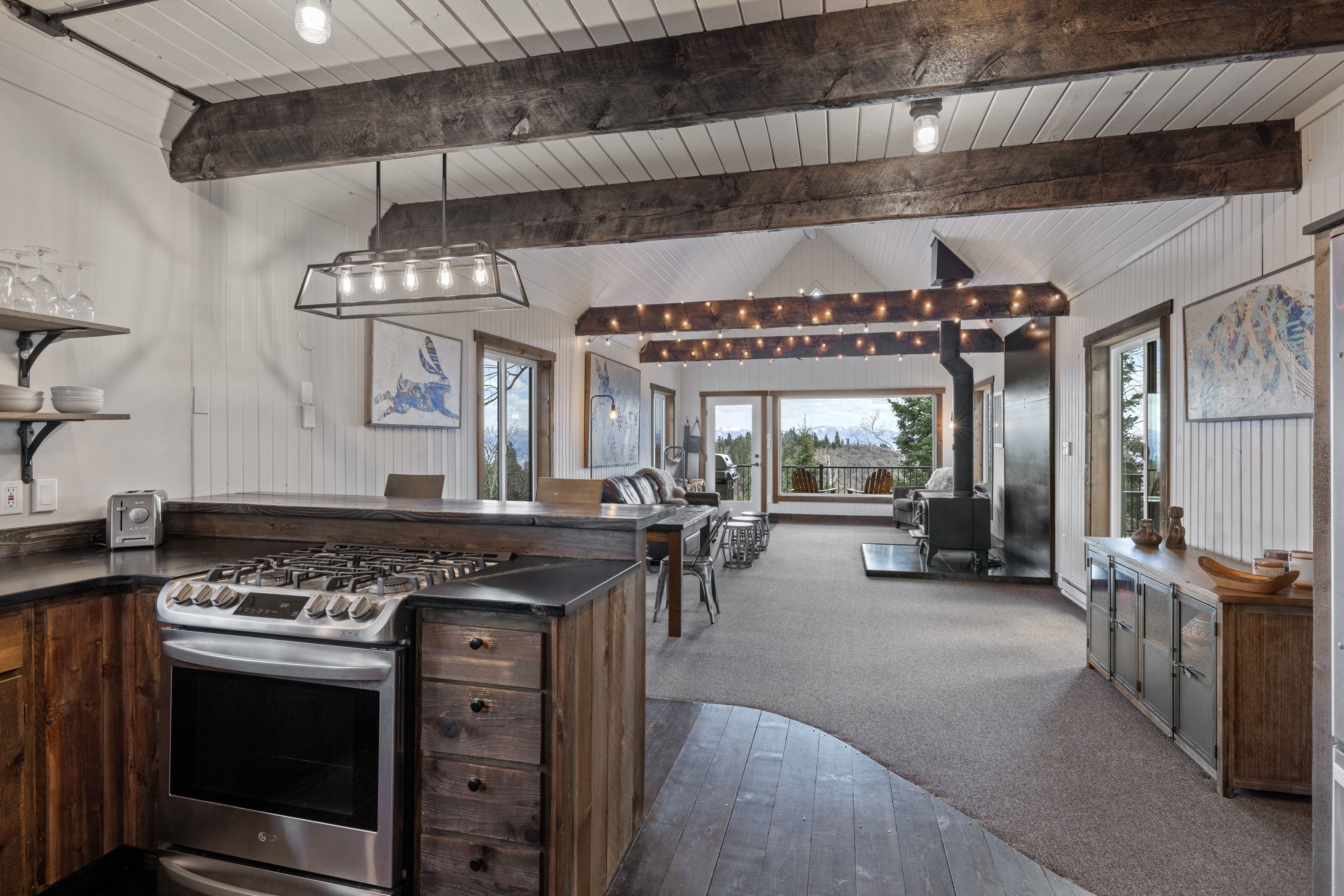 Kitchen with stainless steel gas range oven, a peninsula, open floor plan, a wood stove, and dark colored carpet