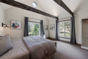 Carpeted bedroom featuring beam ceiling, multiple windows, and wooden walls