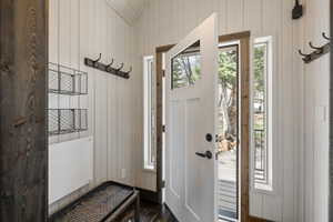 Foyer entrance with wood walls, healthy amount of natural light, dark wood finished floors, and vaulted ceiling