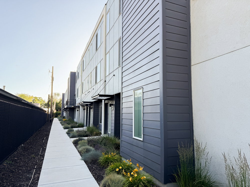 Modern multi-story building featuring dark gray horizontal siding and white stucco accents