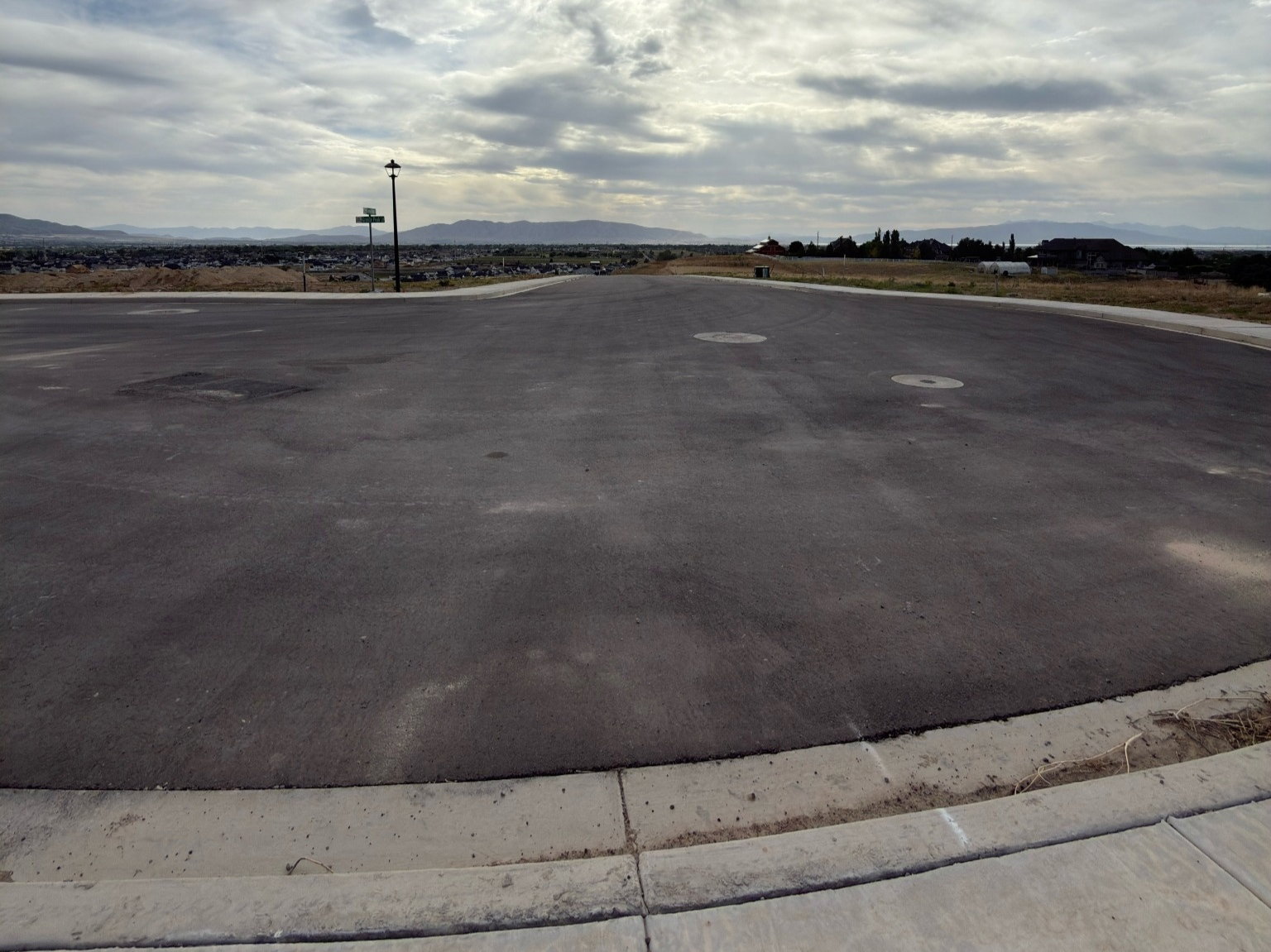 Paved cul-de-sac with concrete curbing and sidewalk, featuring distant mountain scenery and a streetlamp