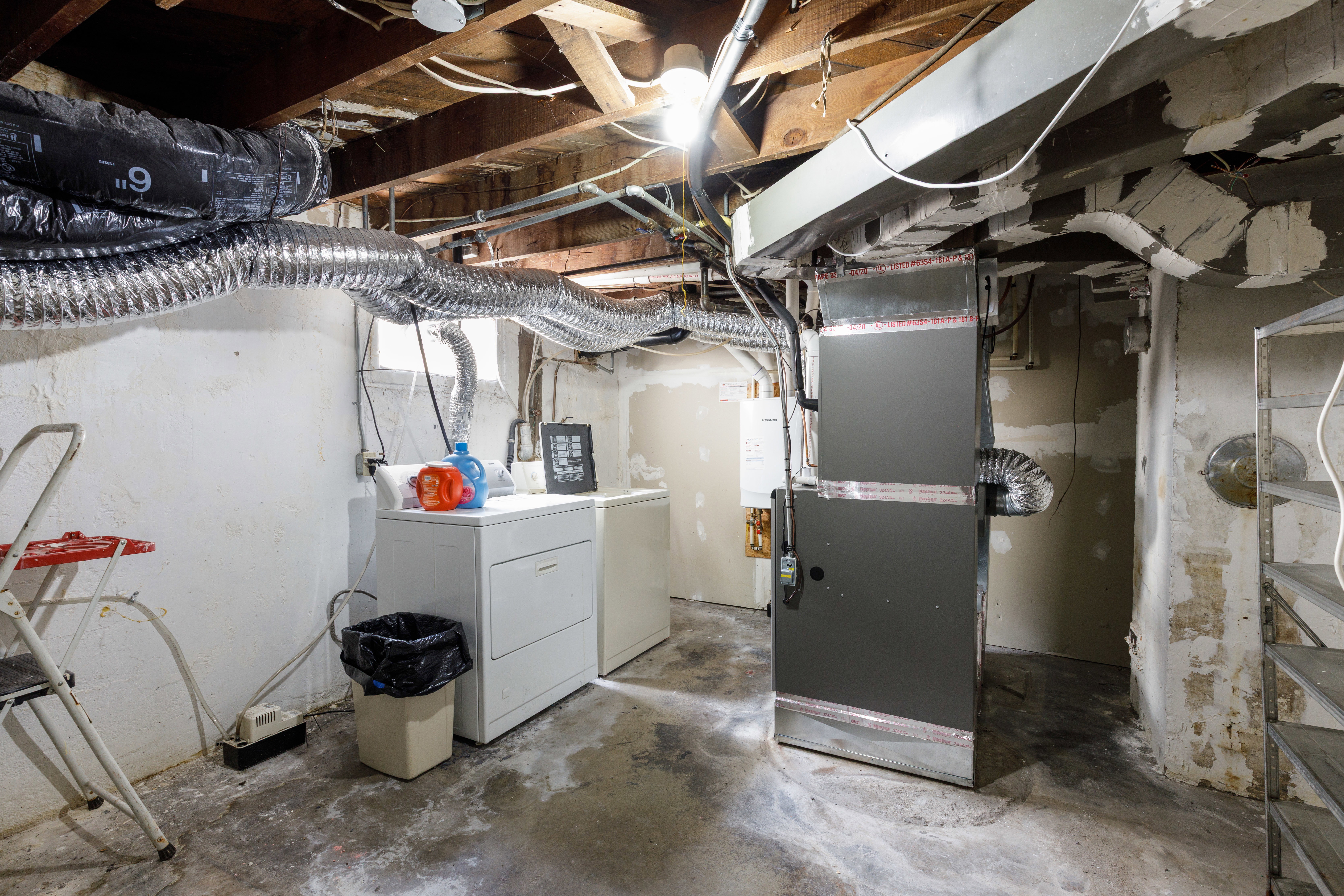 Basement utility room featuring exposed ceiling joists, white painted concrete walls, and concrete flooring