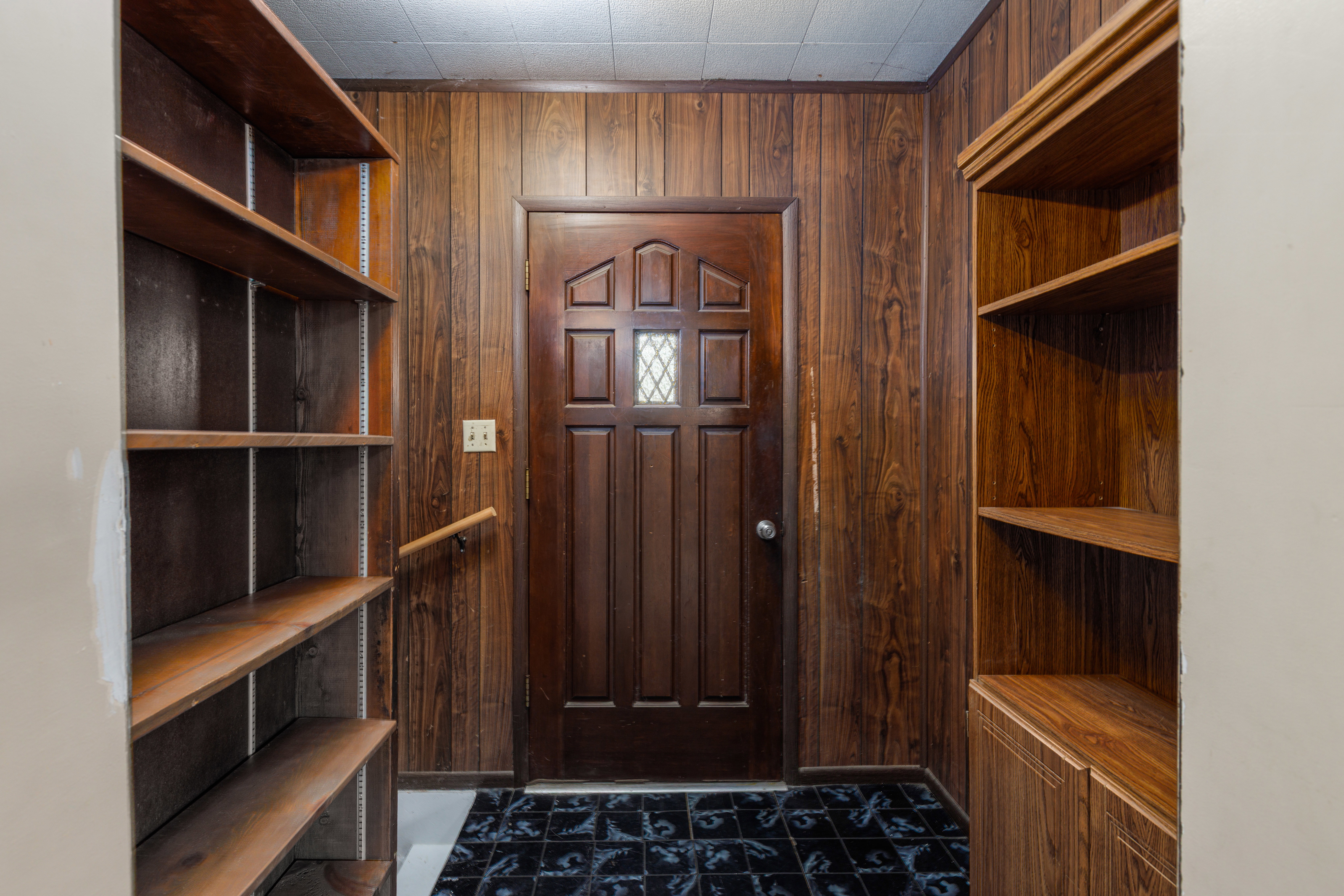 Entryway featuring wood paneling, a paneled door with a decorative glass insert, and built-in shelving units