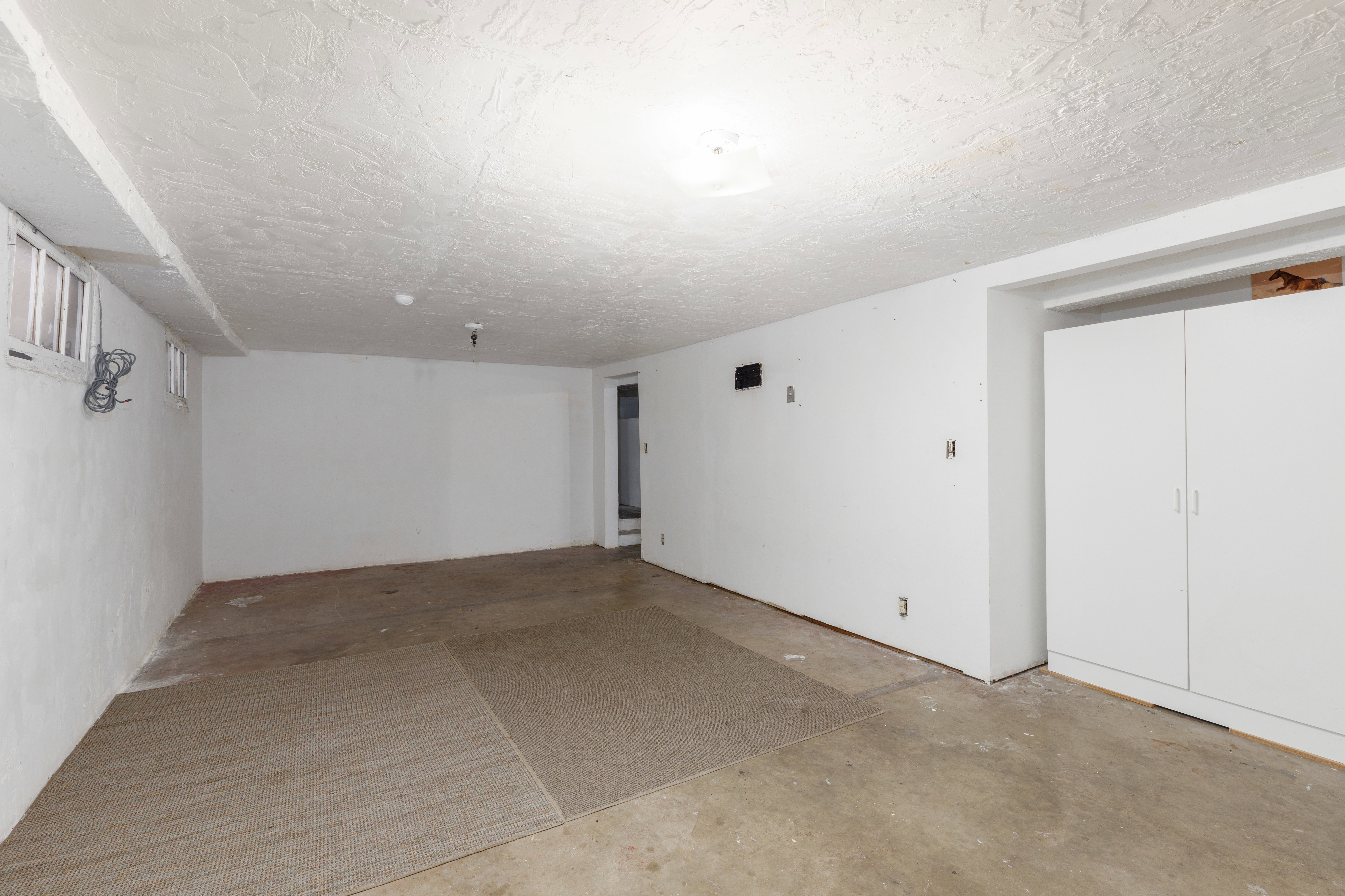 Spacious room featuring light-colored walls, a textured ceiling, and built-in white cabinetry providing storage