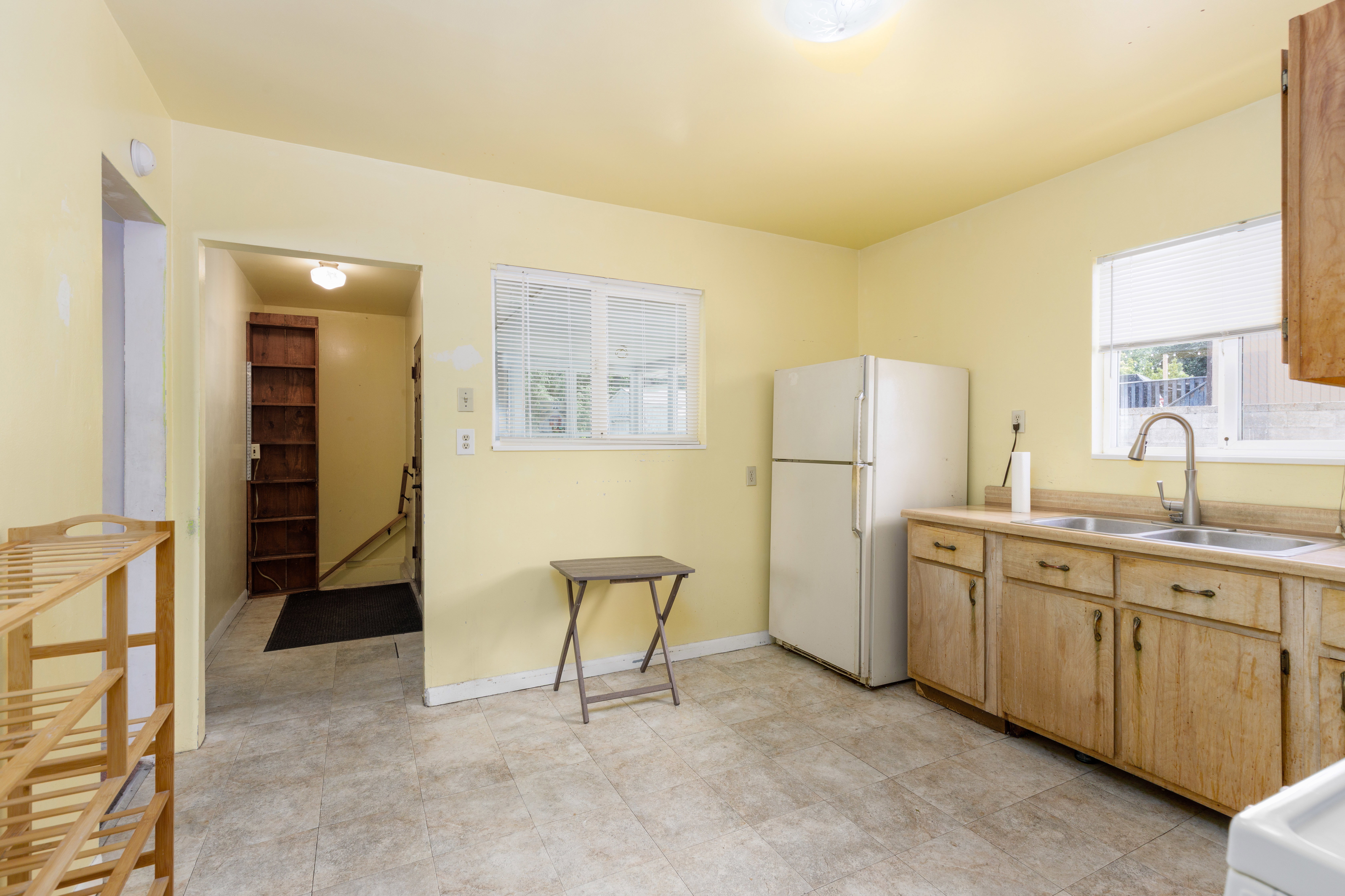 Kitchen area with light-toned tiled flooring, light yellow painted walls, and two windows with horizontal blinds
