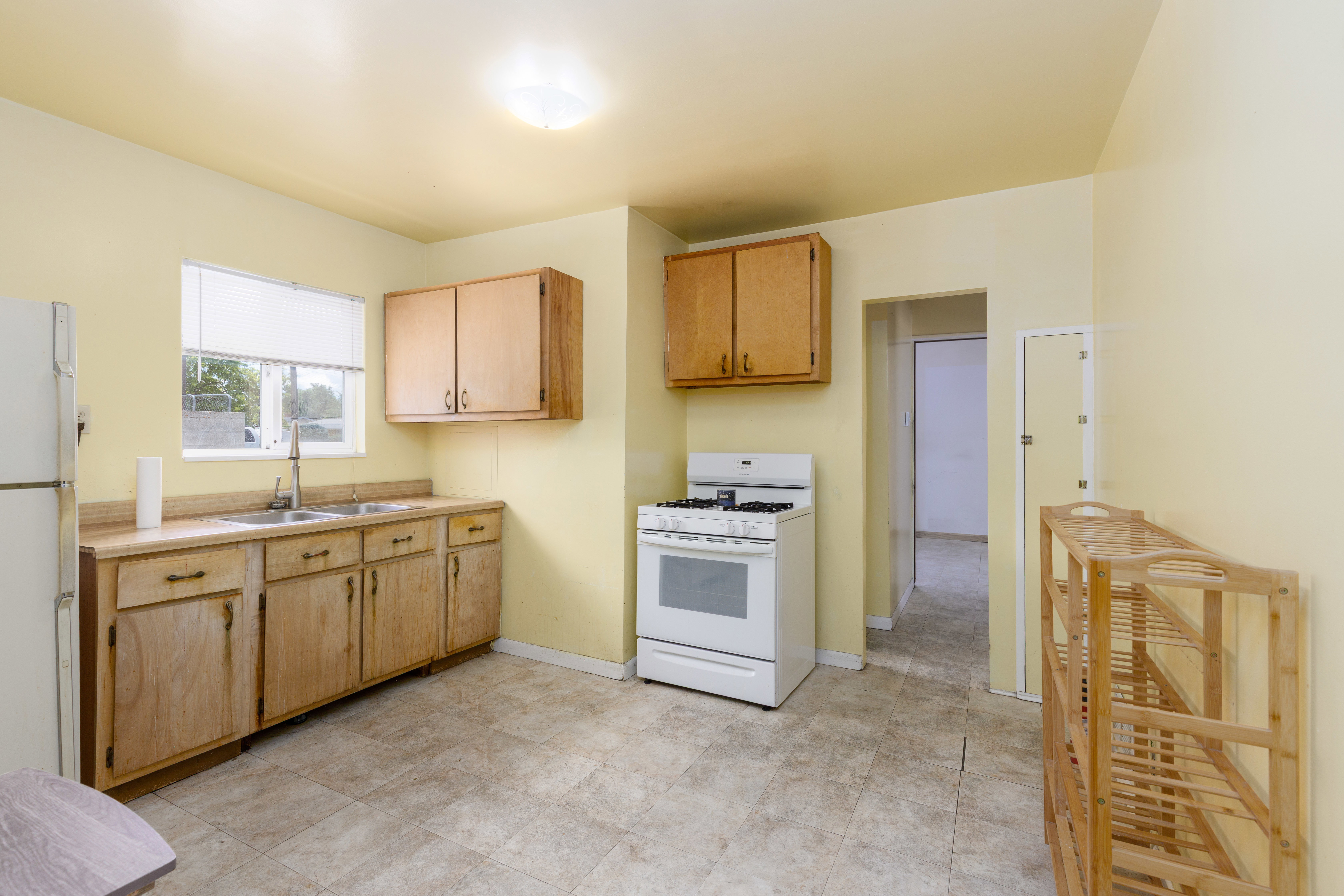 Kitchen featuring wood cabinetry, laminate countertops, a double-basin stainless steel sink with a gooseneck faucet, a freestanding white range, and tiled flooring
