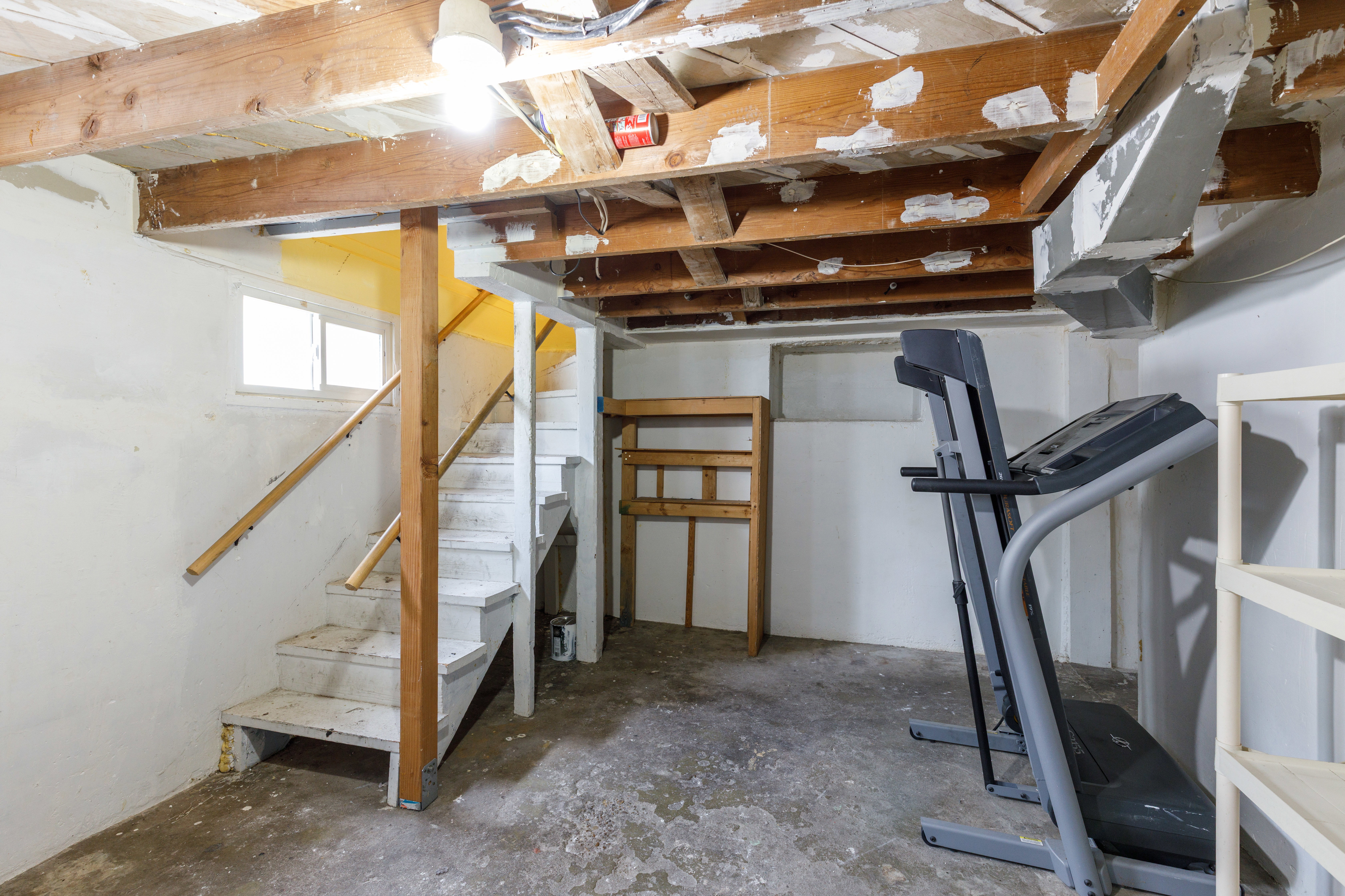 Unfinished basement featuring exposed wood ceiling joists, concrete flooring, and a painted wooden staircase with railing