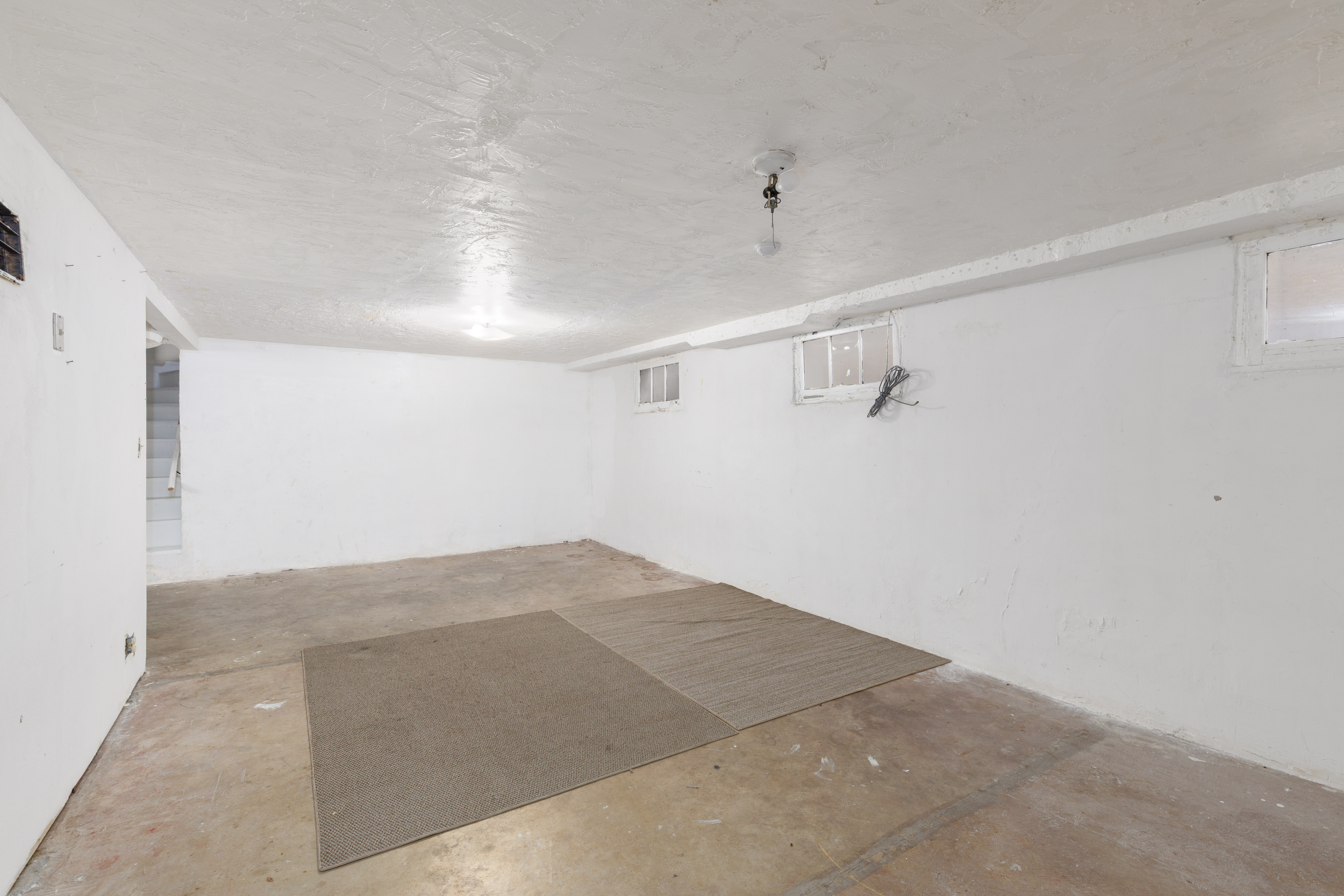 Spacious lower-level room featuring painted concrete flooring, white painted walls, and overhead lighting