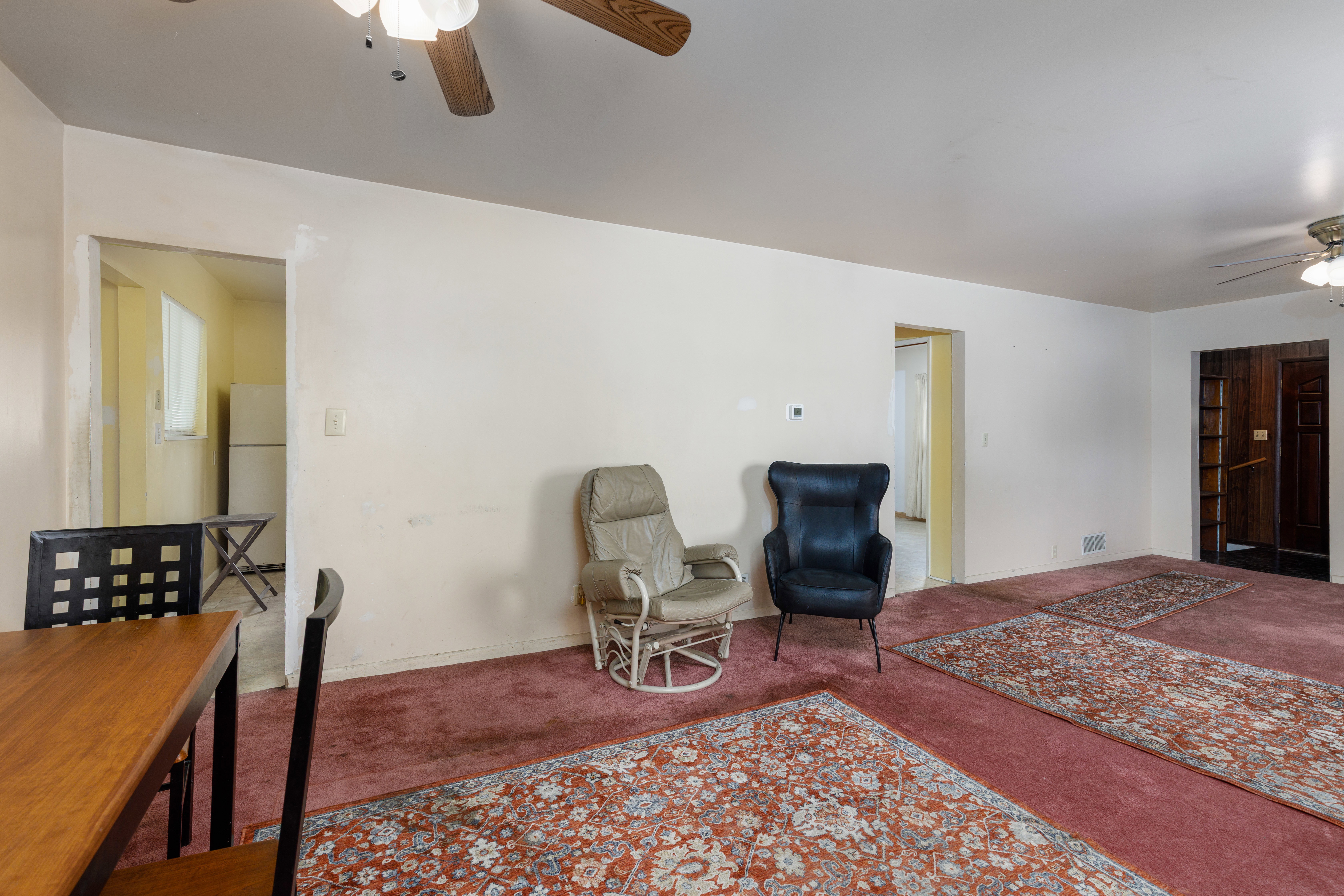 Expansive living area featuring red carpeting, white walls, and a ceiling fan with integrated lighting