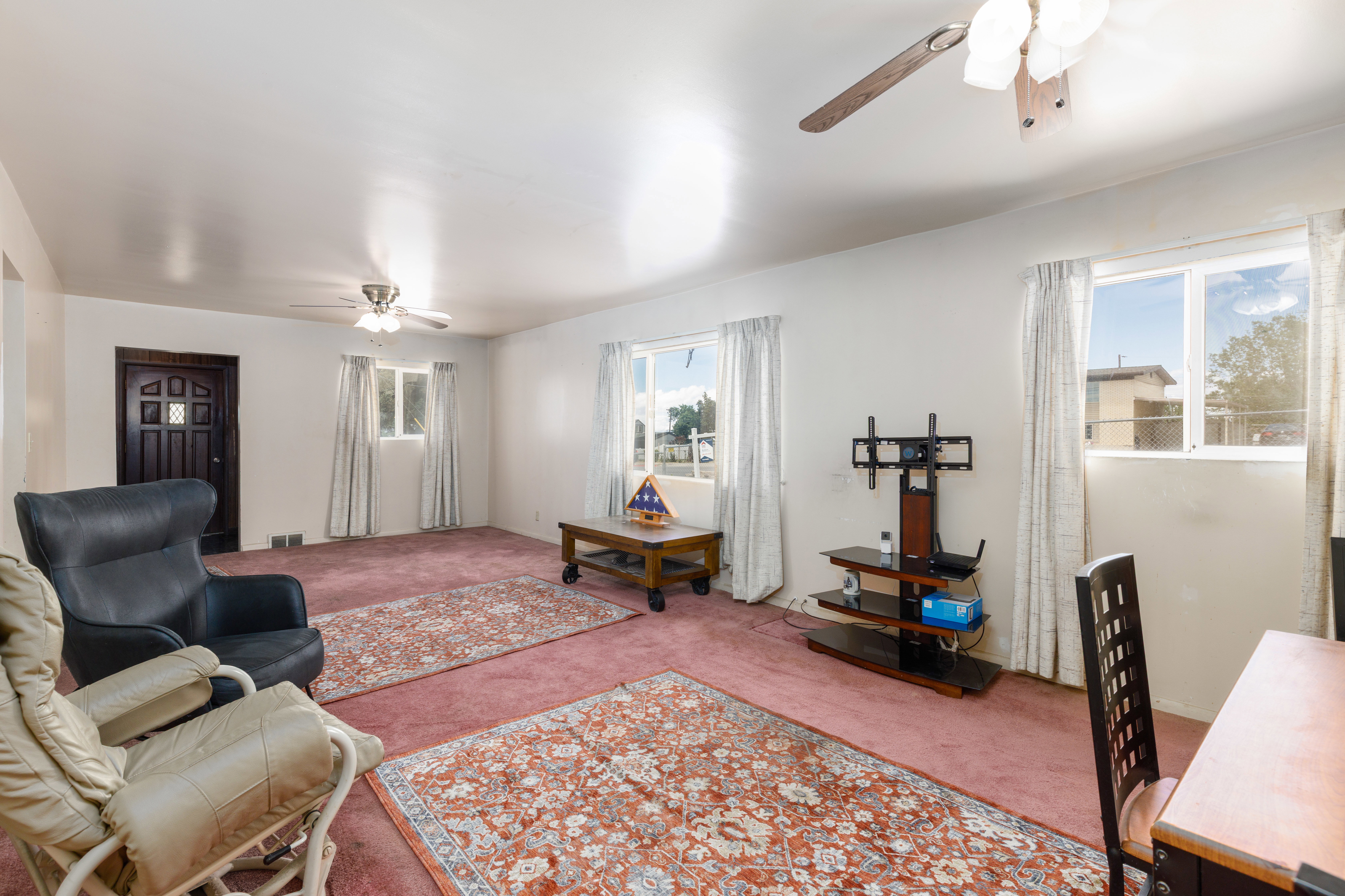 Spacious living area featuring wall-to-wall carpeting, multiple windows for natural light, and two ceiling fans