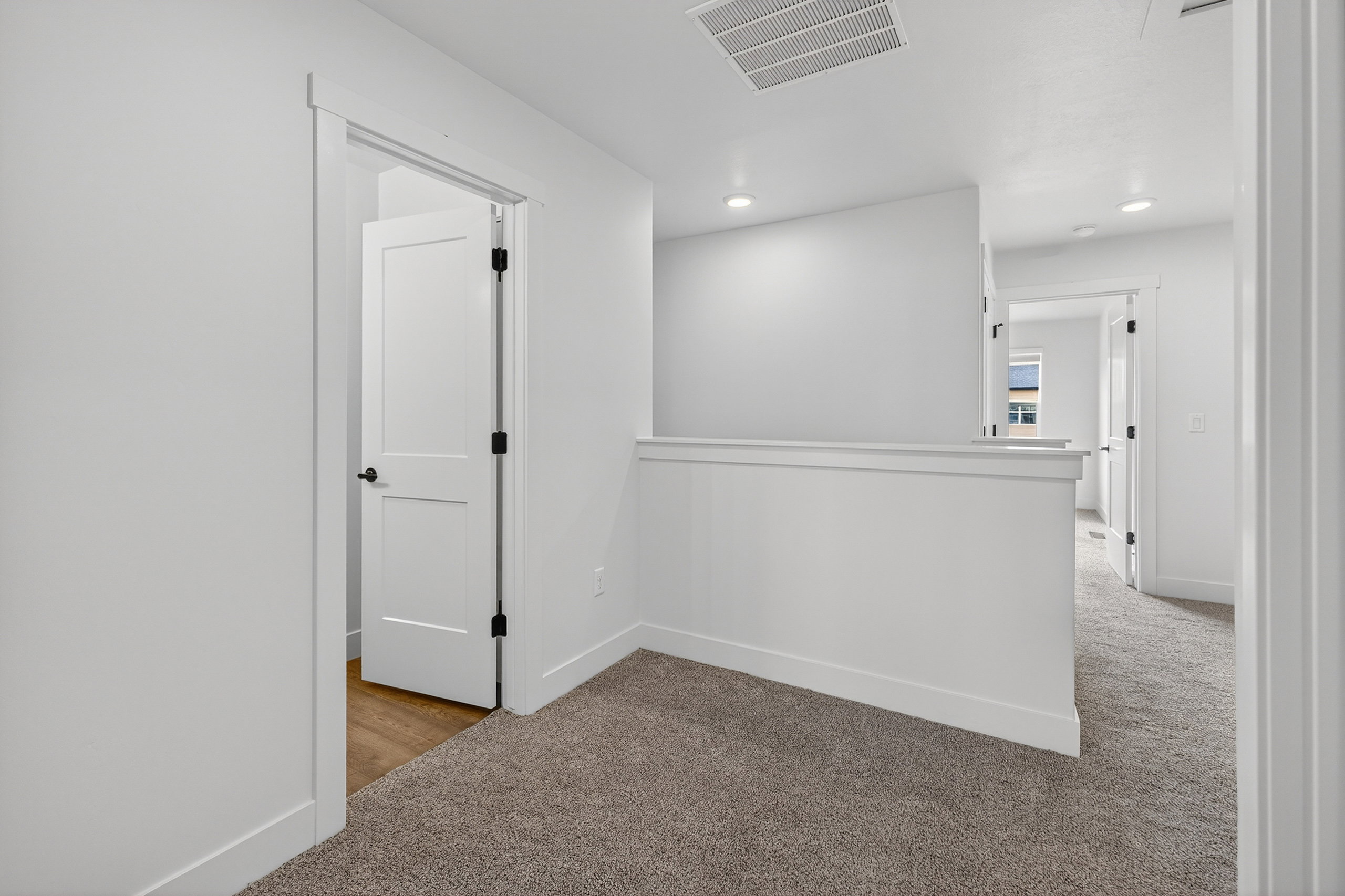 Carpeted hallway featuring white walls, white trim, recessed lighting, and a white interior door with black hardware
