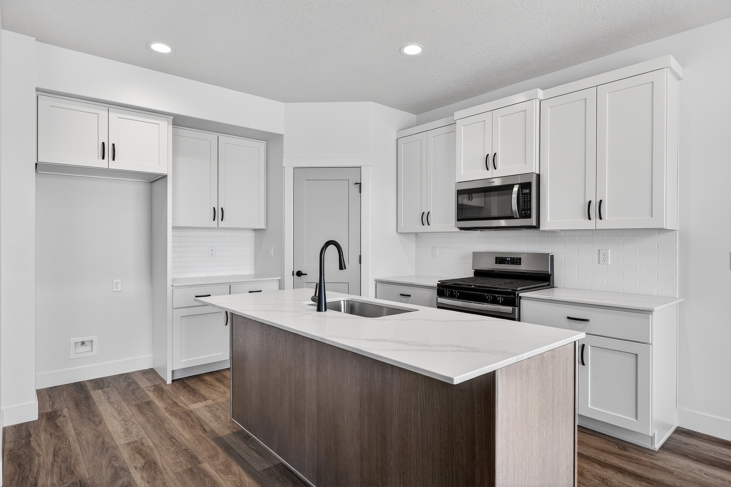 Modern kitchen featuring a two-tone island with a built-in sink, stainless steel appliances, white shaker-style cabinetry, and wood-finish flooring