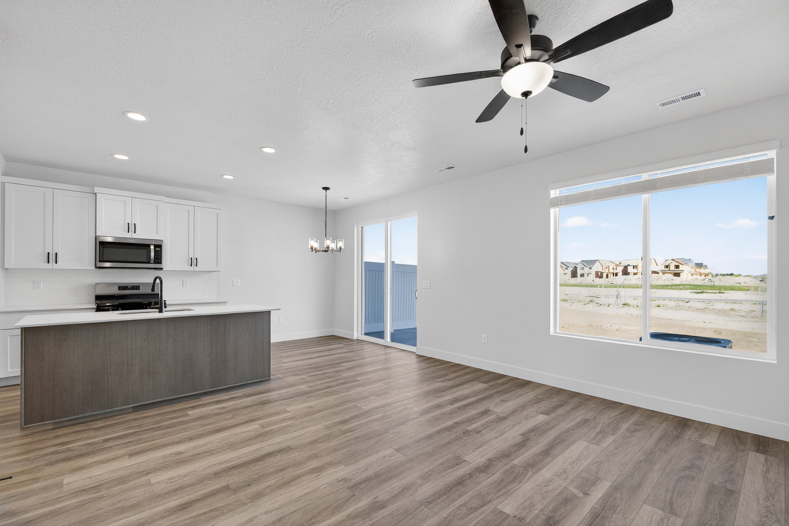Open-concept living area featuring wood-finish flooring, a contemporary kitchen island with a dark wood-tone base, white upper cabinetry, stainless steel appliances, and a glass sliding door to the exterior