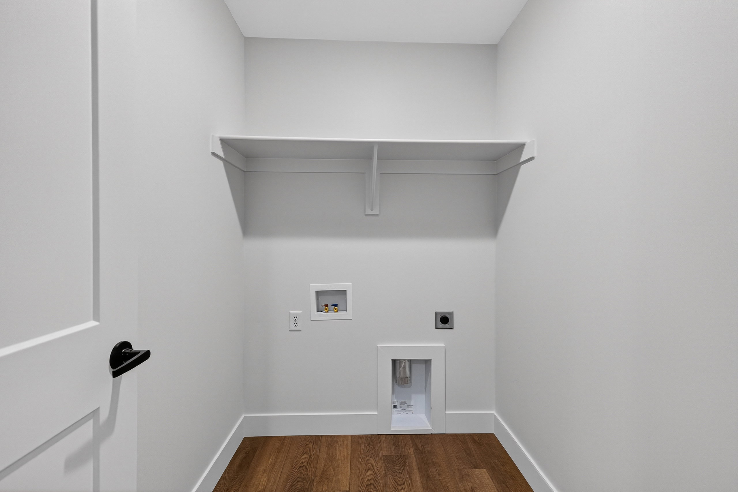 Dedicated laundry area featuring a built-in shelving unit, wood-finish flooring, and white baseboards