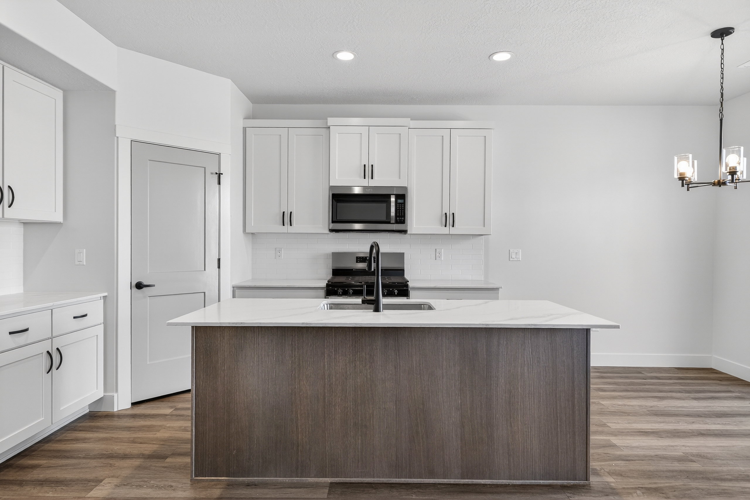 Contemporary kitchen featuring a two-toned island with a light-toned countertop, white cabinetry with black hardware, wood-finish flooring, stainless steel appliances, and a subway tile backsplash