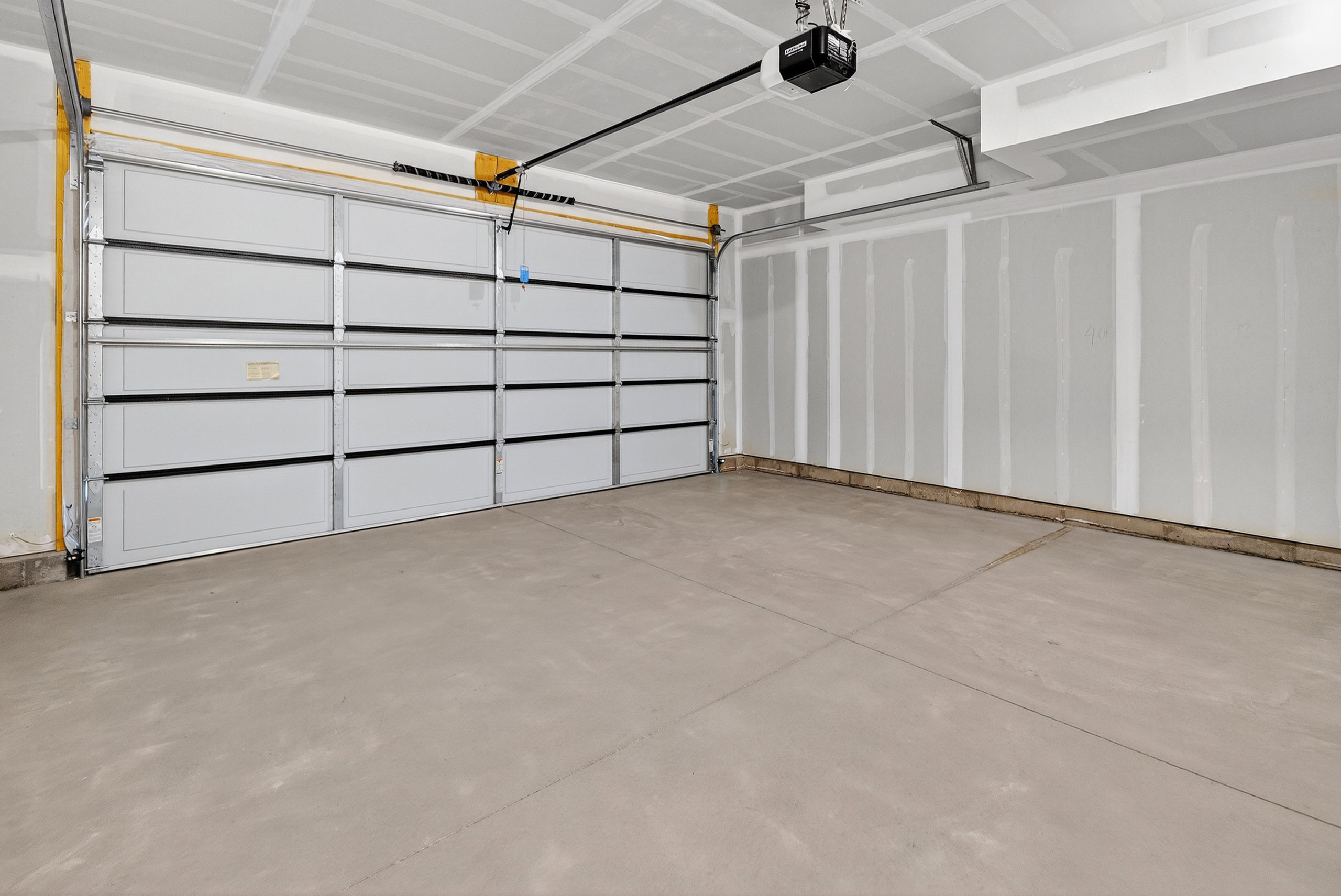 Spacious garage with a light gray sectional garage door, concrete flooring, and unfinished drywall walls