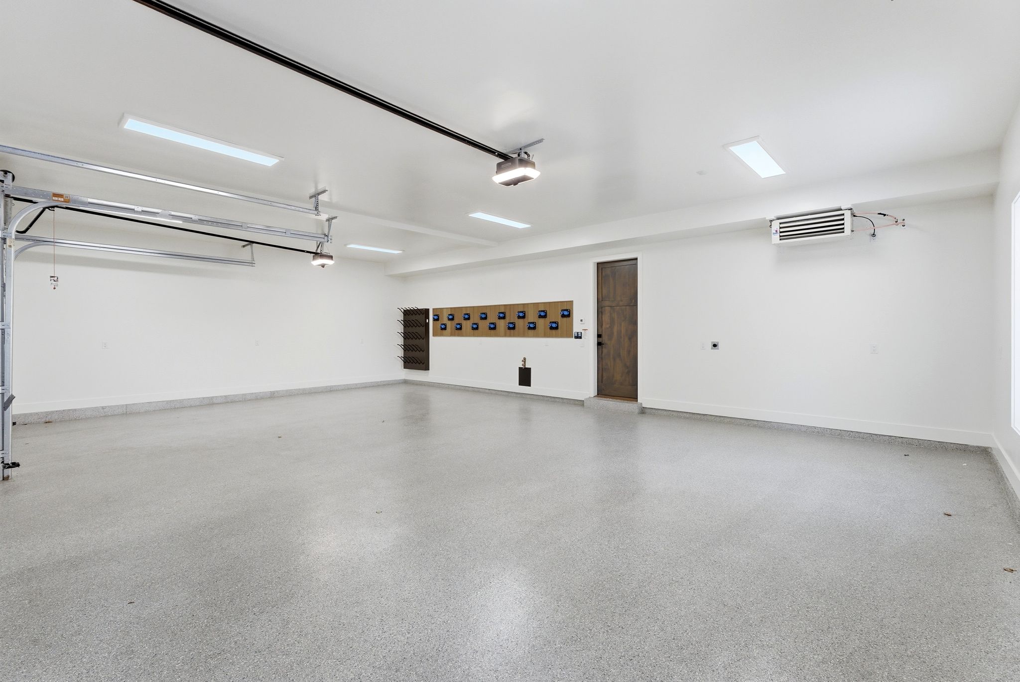 Spacious garage featuring epoxy flooring, crisp white walls, recessed fluorescent lighting, an industrial-style heater, and a dark wood-finish door