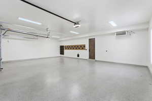 Spacious garage featuring epoxy flooring, crisp white walls, recessed fluorescent lighting, an industrial-style heater, and a dark wood-finish door