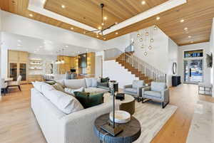 Open-concept living area featuring light wood-finish flooring, a two-story ceiling with recessed lighting and wood panel accents, and a built-in kitchen with integrated appliances
