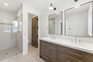 Bathroom featuring a glass-enclosed shower with subway tile surround, a dual vanity with a white countertop and wood-finish cabinetry, two rectangular framed mirrors, and light tile flooring