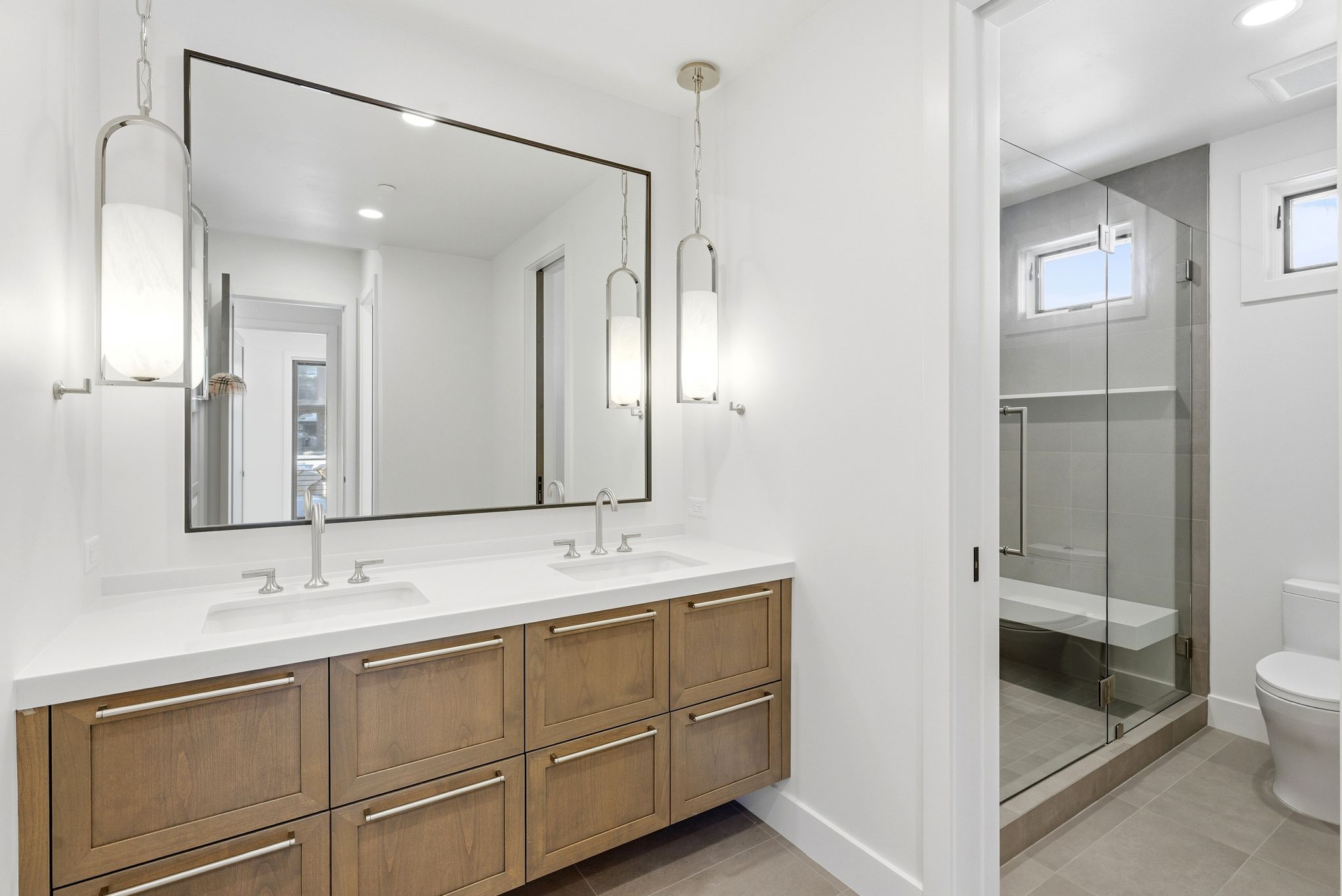 Double vanity featuring undermount sinks, contemporary wall-mounted light fixtures, and a spacious framed mirror