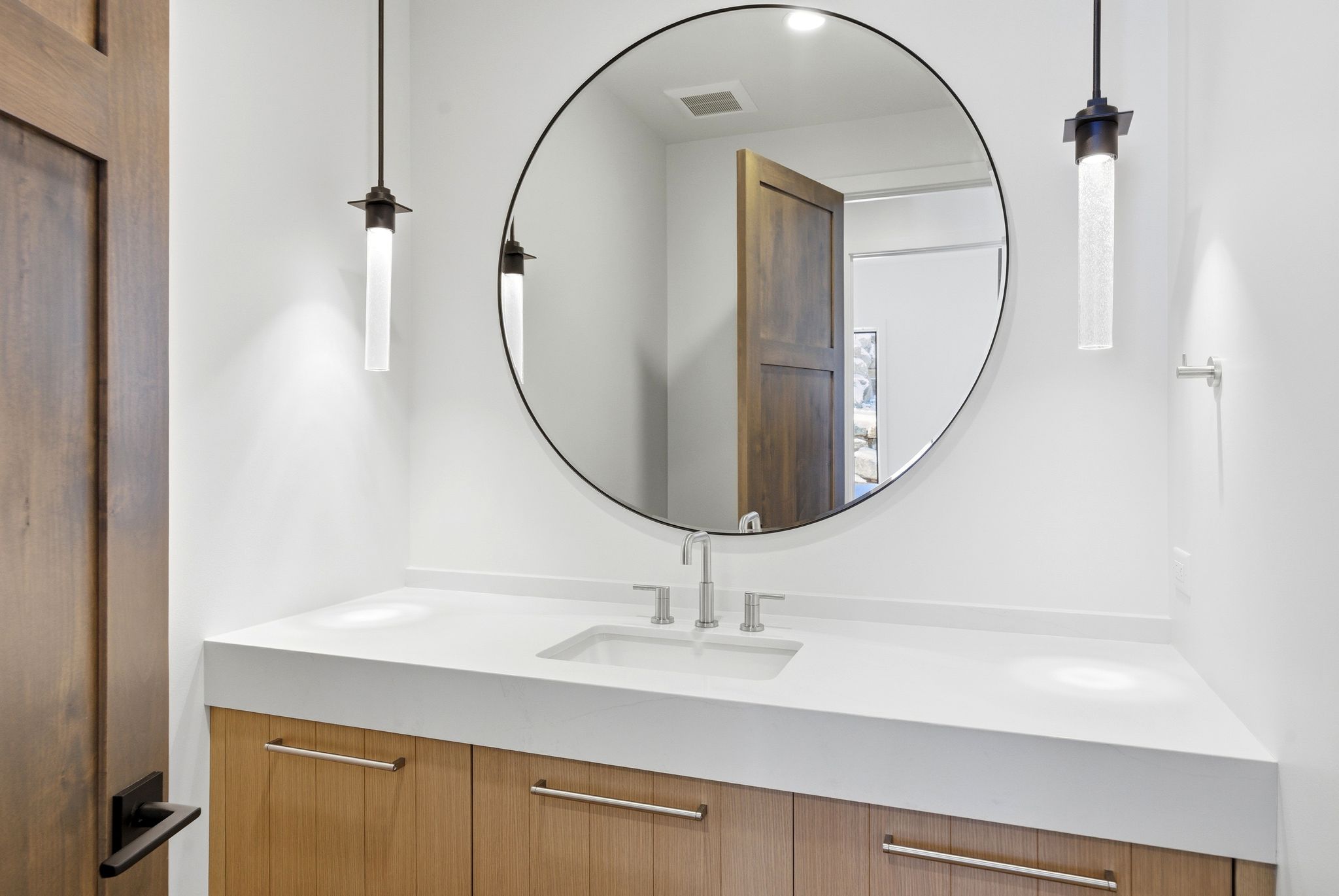 Vanity with light wood-finish cabinetry, a white countertop, and an undermount sink