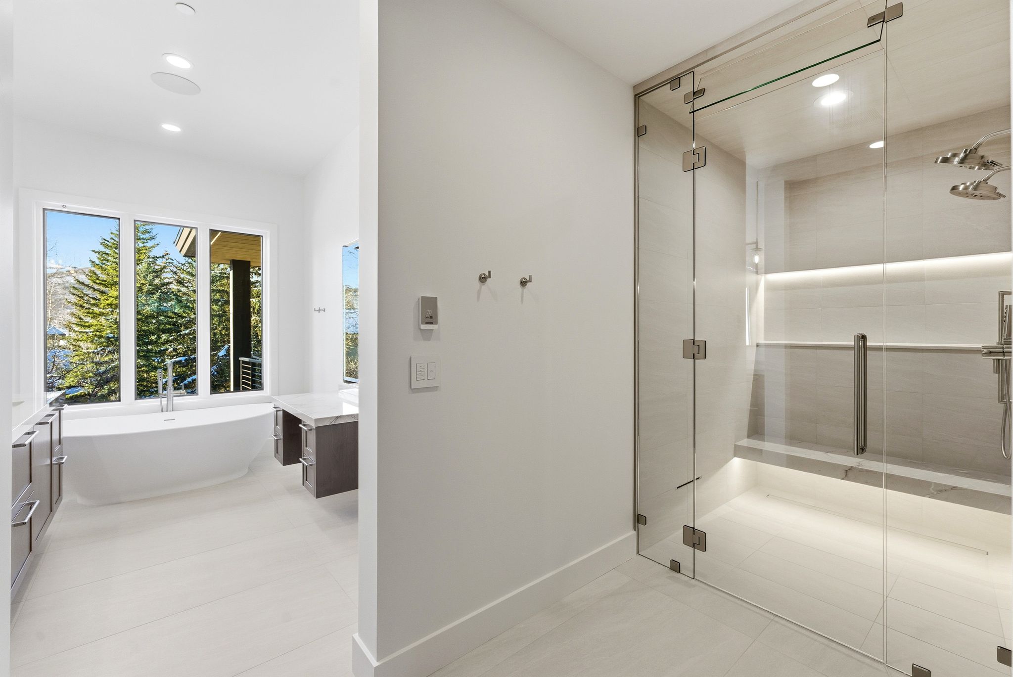Contemporary bathroom featuring a spacious glass-enclosed shower with multiple showerheads, an integrated bench, and accent lighting