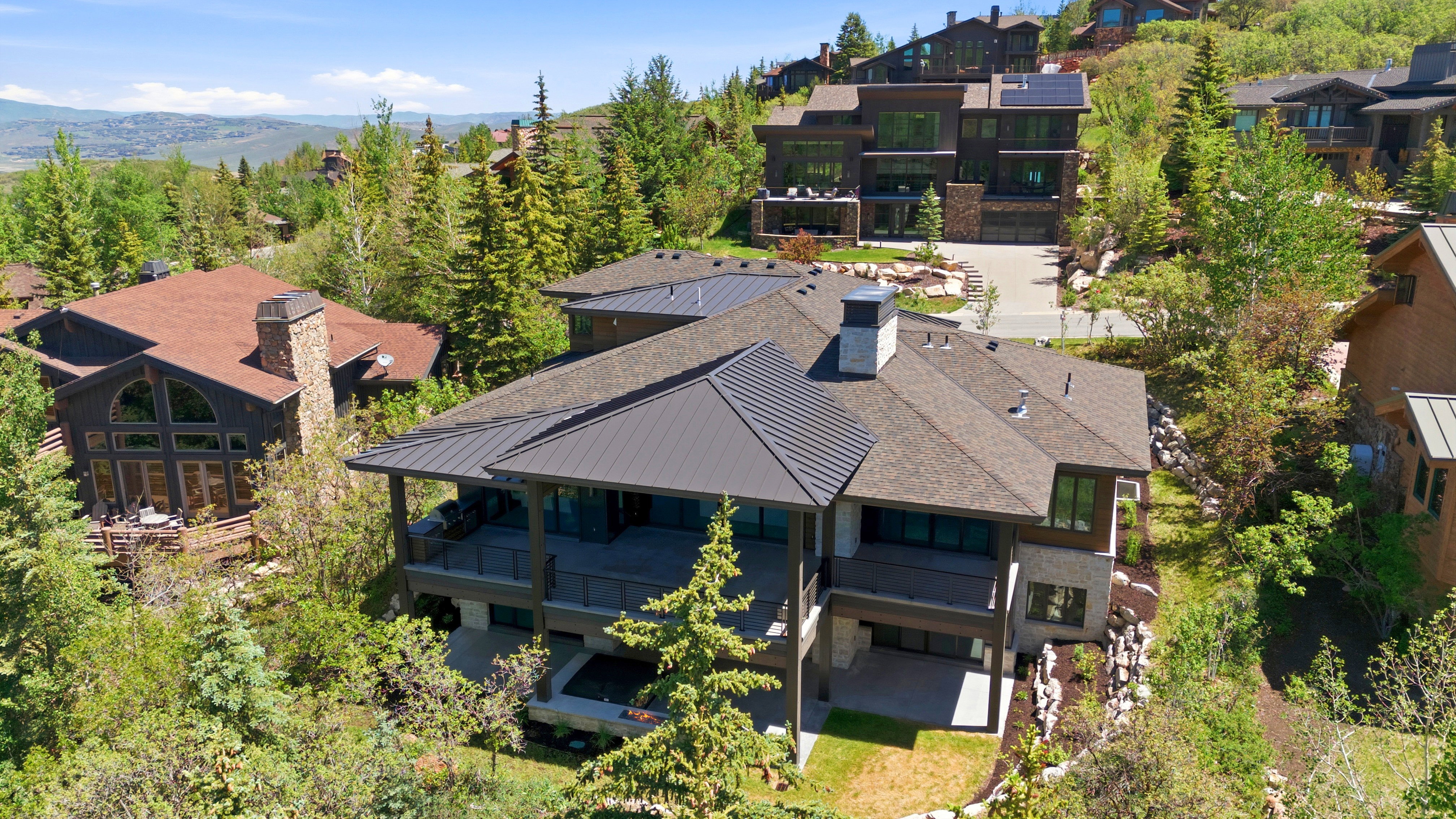 Multi-level residence featuring a dark metal standing seam roof, shingle roof, and stone accents