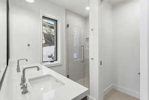 Bathroom featuring a dual vanity with integrated sinks and wall-mounted faucets, a frameless glass shower enclosure with subway tile surround, a tall vertical window, and light-toned flooring