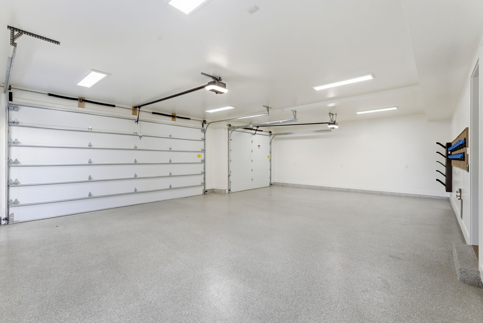 Spacious garage featuring two overhead doors, a speckled epoxy floor, bright overhead lighting, and white painted walls