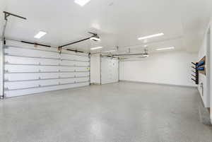 Spacious garage featuring two overhead doors, a speckled epoxy floor, bright overhead lighting, and white painted walls