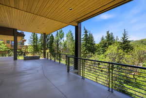 Expansive covered outdoor living area featuring a concrete deck, wood-paneled ceiling, and contemporary cable railing system