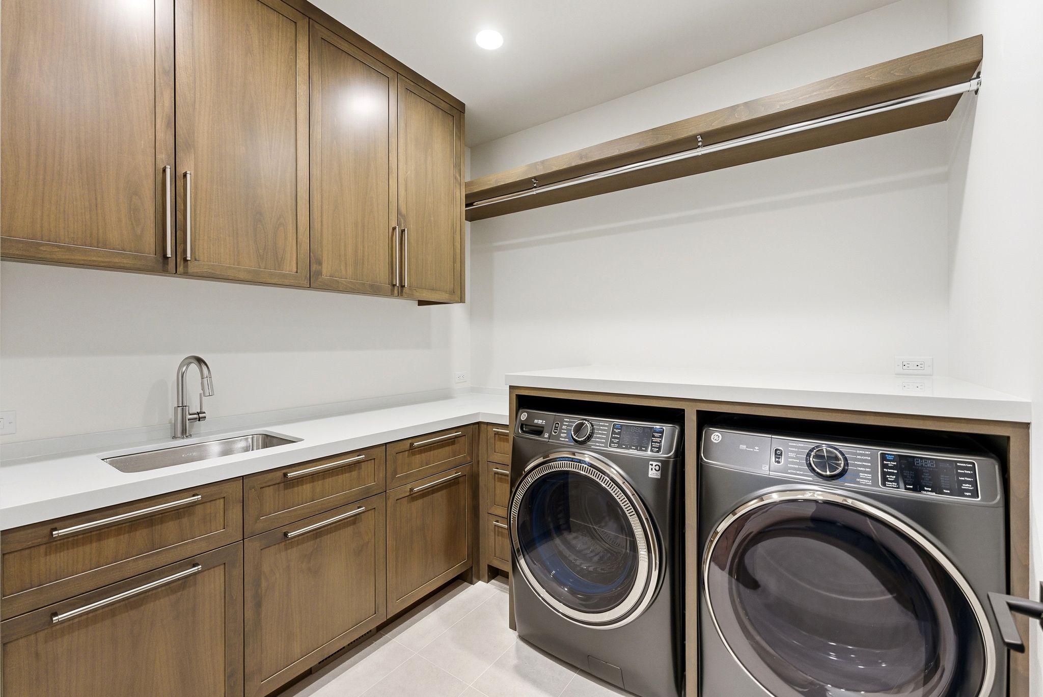Dedicated laundry room featuring wood-finish cabinetry, white countertops, and an undermount sink with a gooseneck faucet