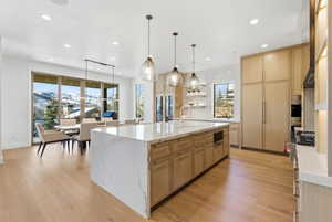 Gourmet kitchen featuring a waterfall island with stone countertop, wood-finish cabinetry, and integrated appliances