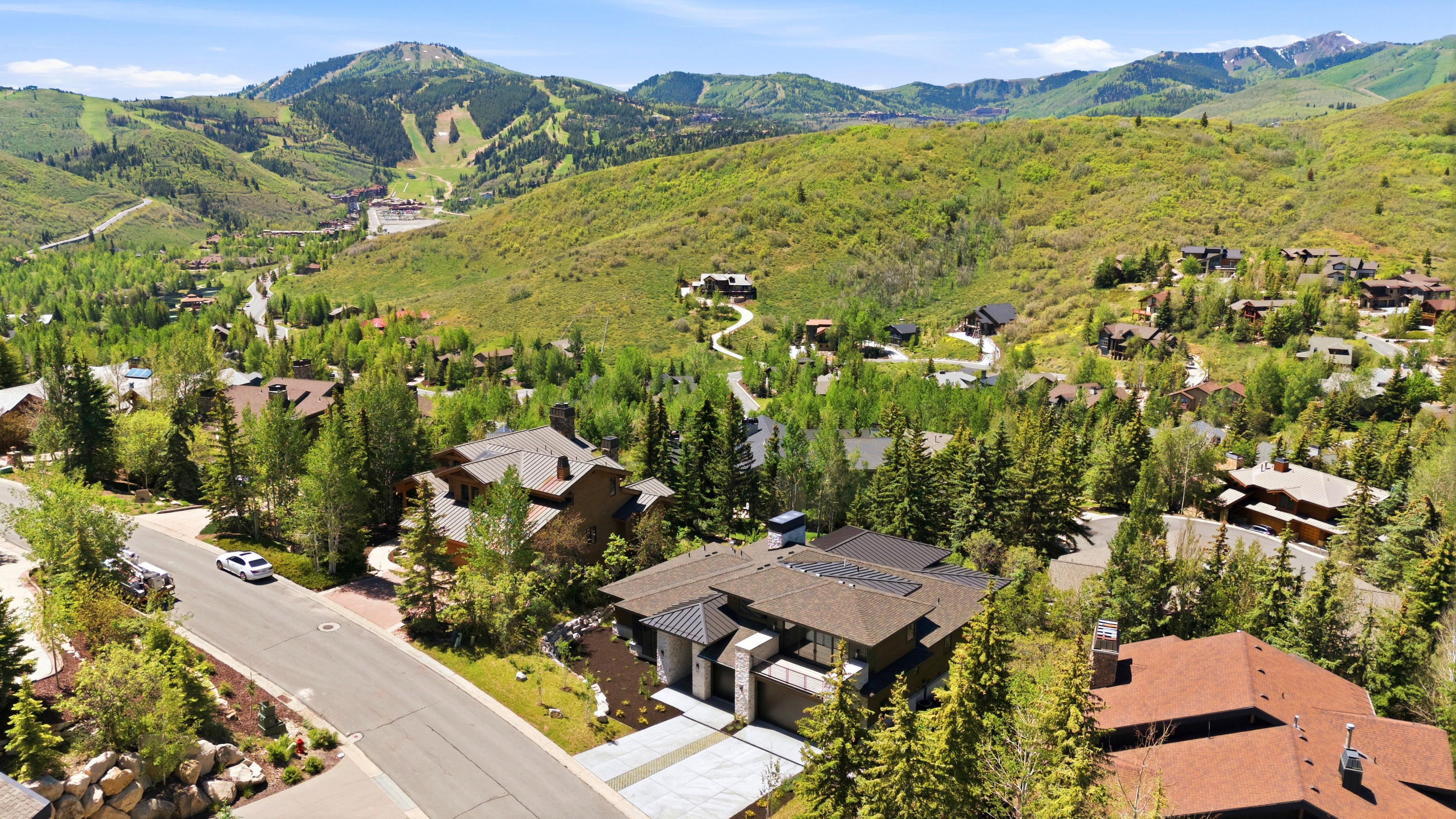 Contemporary mountain residence situated on a paved street, featuring a dark roof, attached garage, and a landscaped front approach
