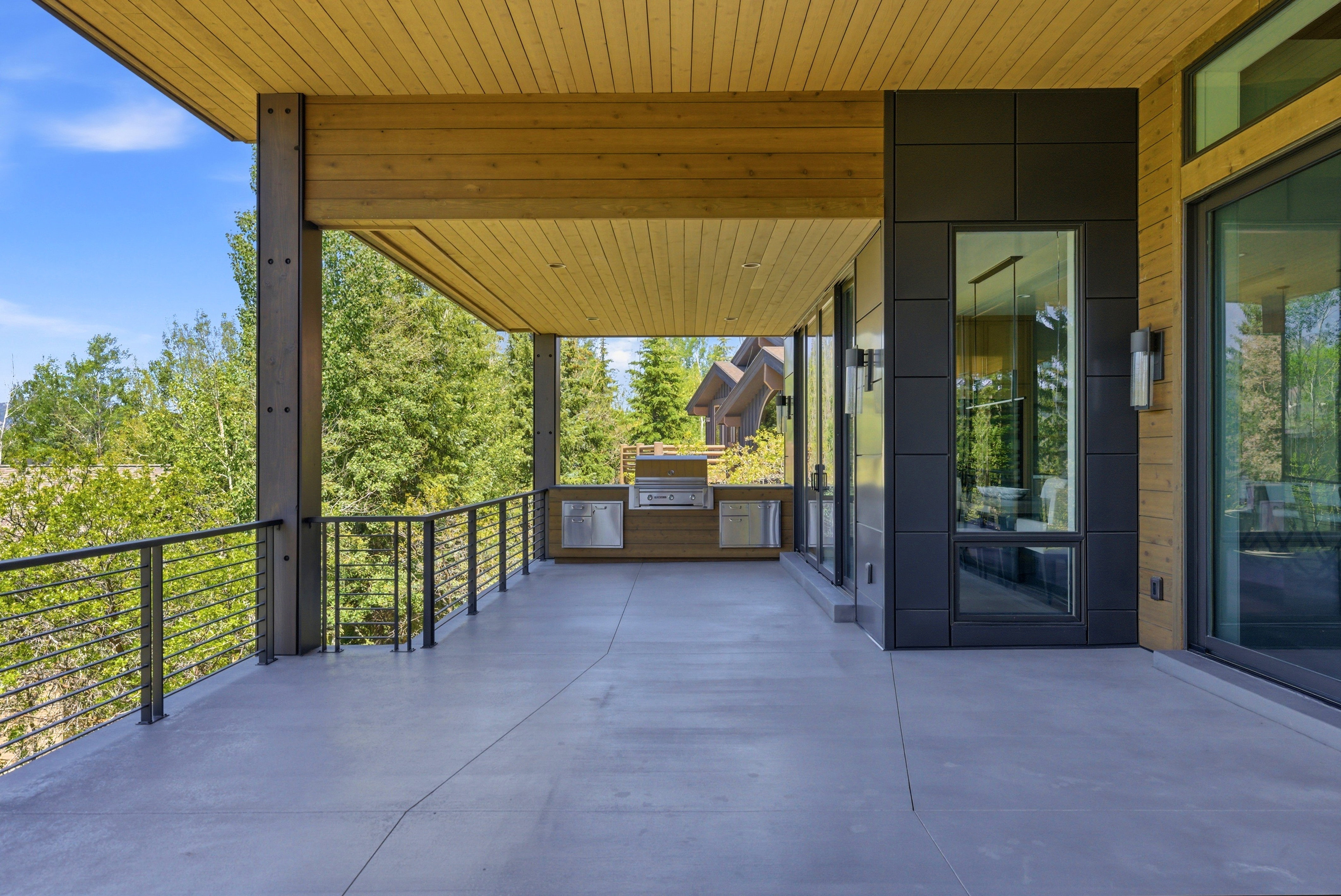 Expansive covered patio featuring a built-in outdoor kitchen, wood-finish ceiling, and cable railing