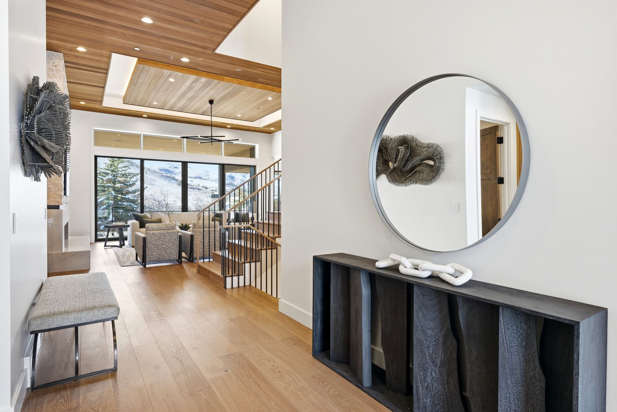 Expansive living area featuring a wood-panel ceiling, large windows with mountain scenery, and light wood-finish flooring