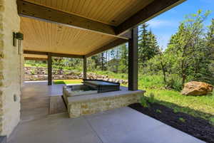 Covered outdoor patio featuring a built-in spa, a stone retaining wall, and natural landscaping