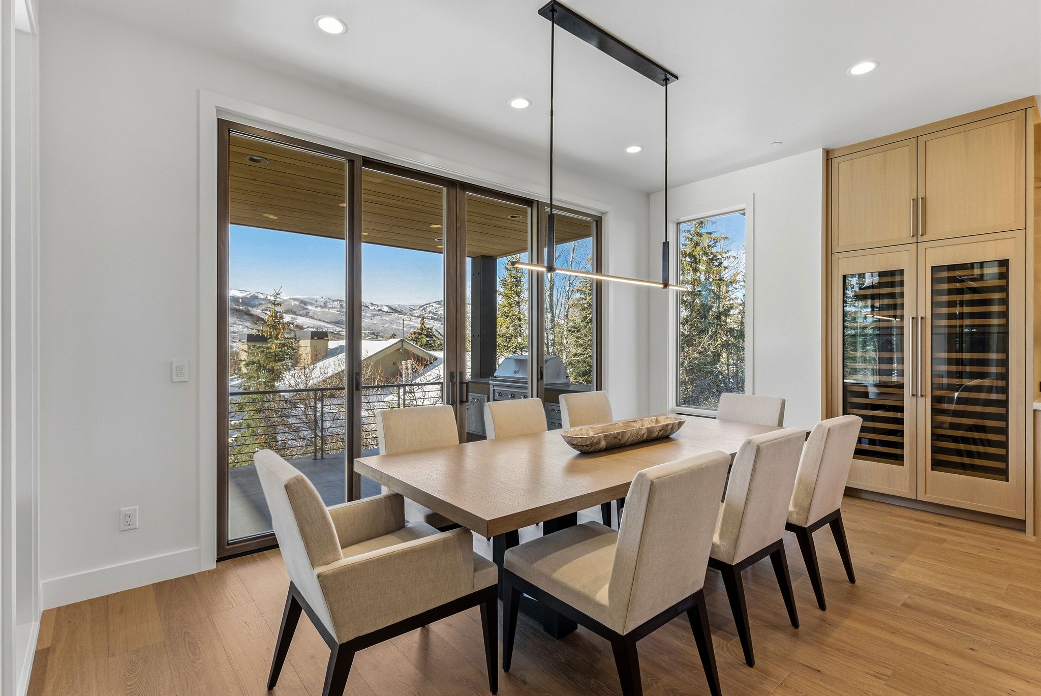 Dining area featuring wood-finish flooring, a linear pendant light fixture, recessed ceiling lights, and built-in cabinetry with integrated wine refrigerators