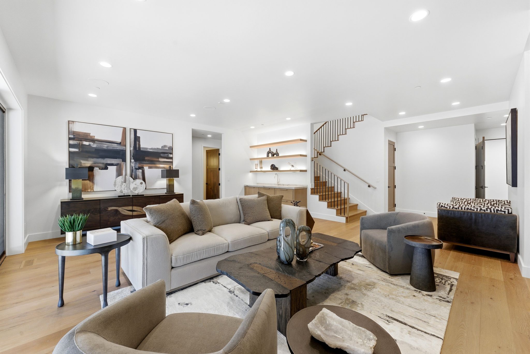 Bright living area featuring wood-finish flooring, recessed lighting, and a contemporary staircase with metal balusters
