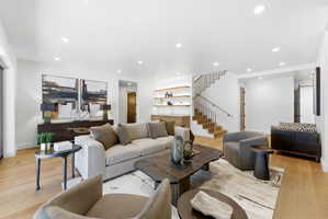 Bright living area featuring wood-finish flooring, recessed lighting, and a contemporary staircase with metal balusters