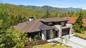 Contemporary mountain residence featuring a multi-gabled roofline, stone and wood-tone exterior accents, a prominent balcony with metal railing, an integrated garage, and a concrete driveway