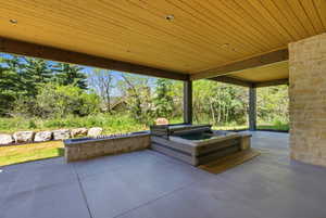 Covered patio featuring a built-in spa, stone retaining wall, and concrete flooring